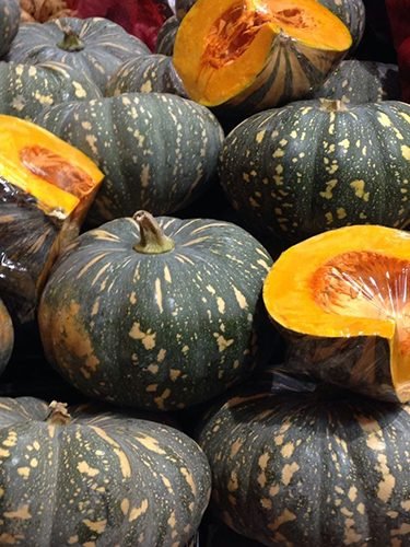 Pumpkins, mottled green skins stacked with two cut open to show the orange flesh